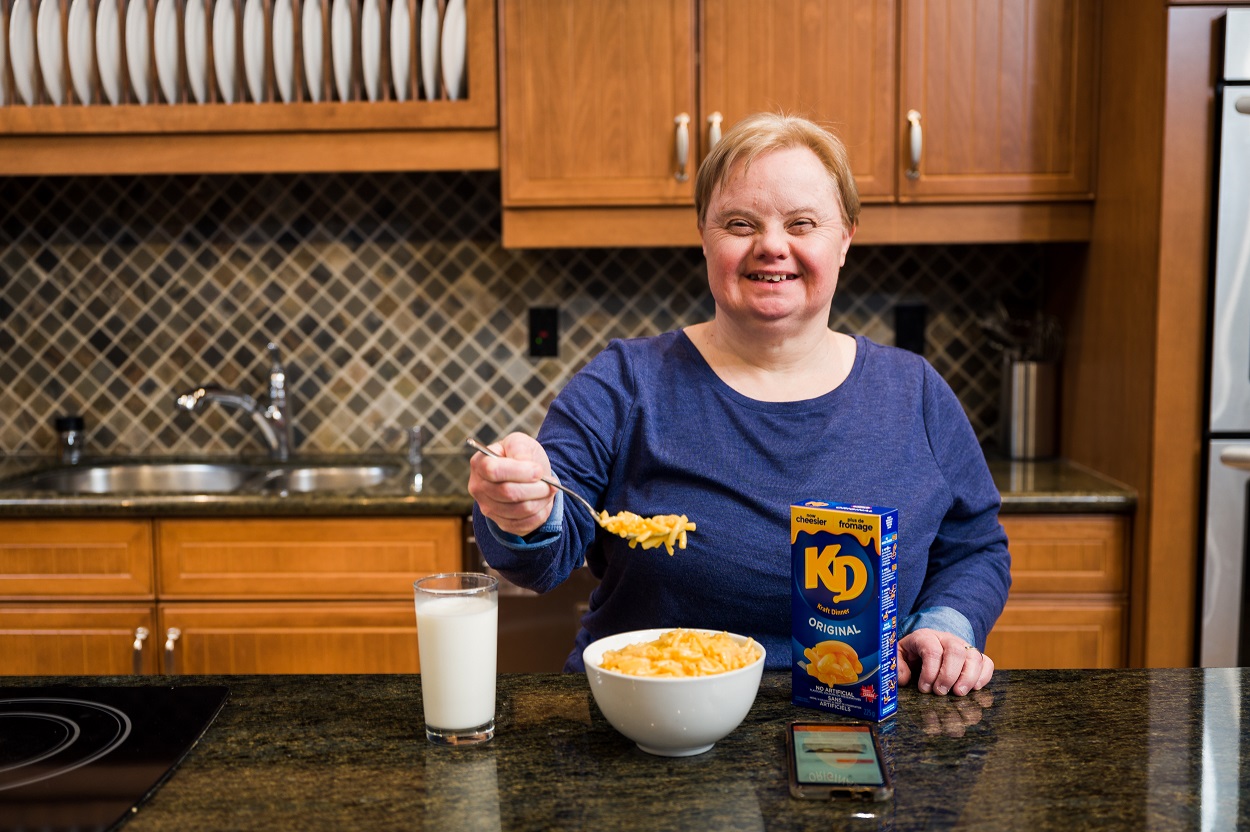 Woman smiling infront of bowl of Kraft dinner in kitchen