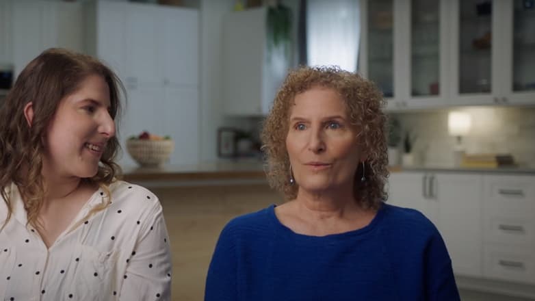 Mom and adult daughter sit side-by-side in kitchen