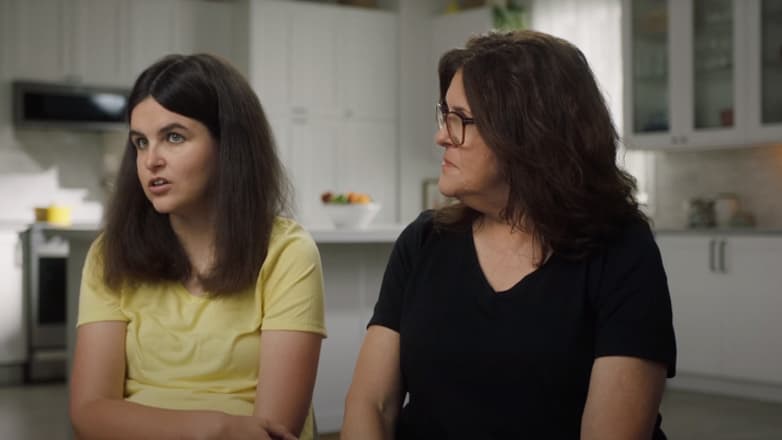 Mom and adult daughter sit side-by-side in kitchen