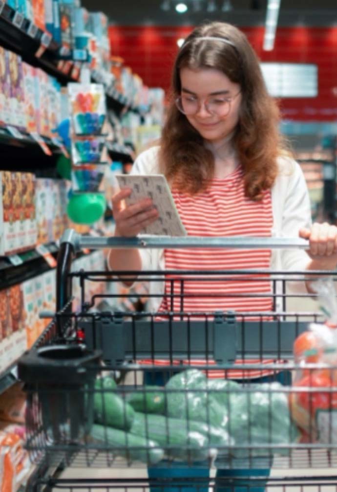 Young lady in grocery store, pushing cart with groceries while looking at her shopping list